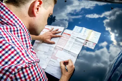 Mężczyzna w kratę wypełnia formularz oświadczenia o kolizji na masce samochodu.